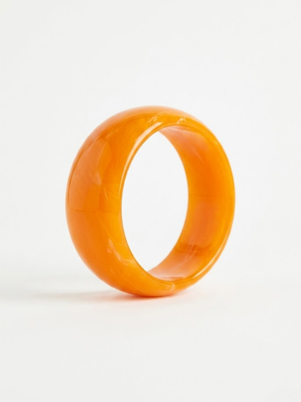 Primer plano de brazalete rígido ancho de estilo argolla en color naranja vibrante con efecto traslúcido y acabado pulido liso de Angel Salvaje.
