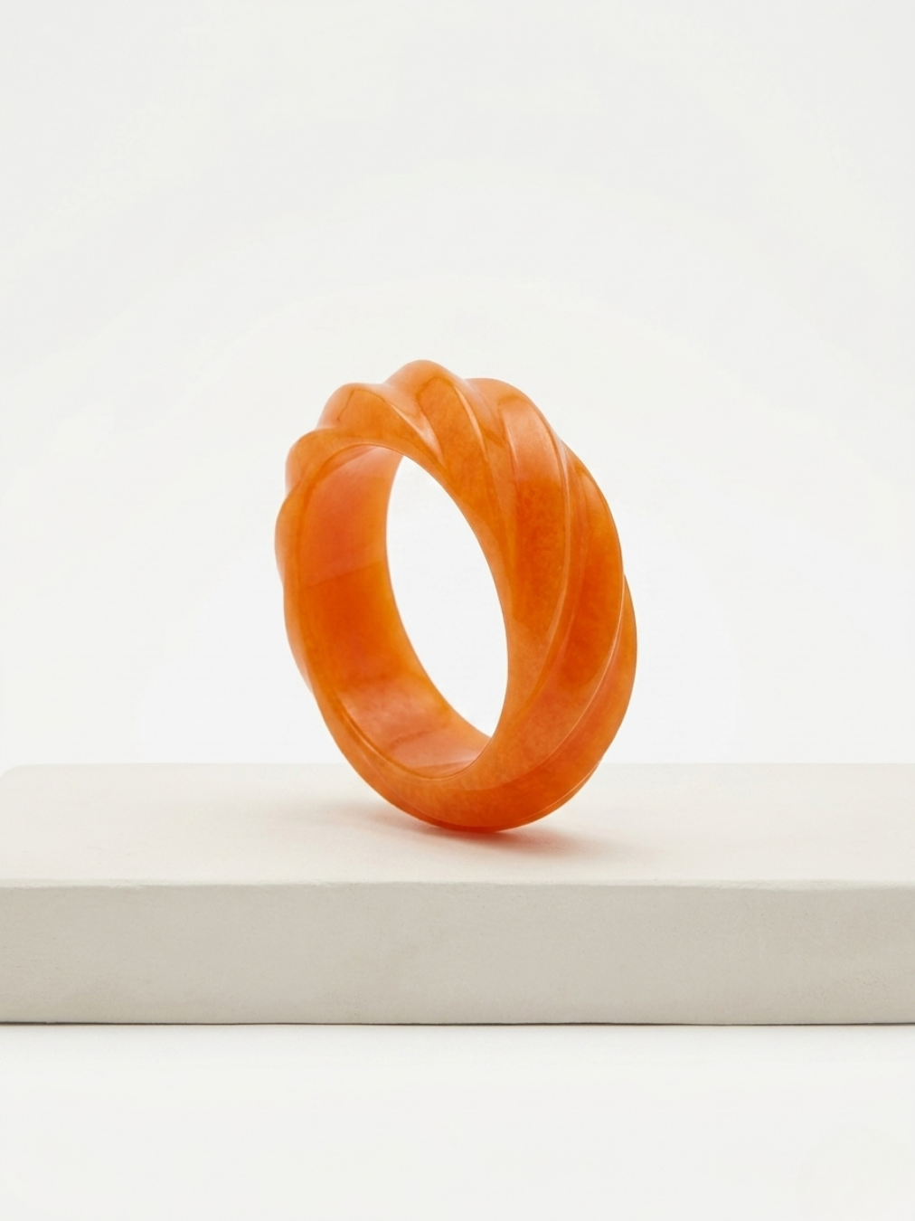 Primer plano de brazalete rígido ancho en color naranja vibrante con relieve de ondas en espiral y acabado pulido traslúcido de Ángel Salvaje.