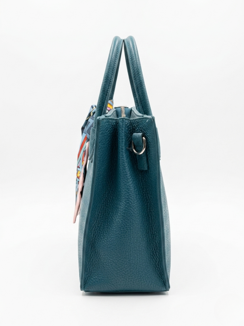 Perfil lateral del bolso structural color azul petróleo con el detalle del pañuelo estampado anudado en el herraje.