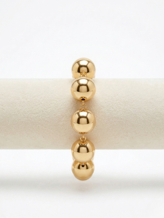 Primer plano de brazalete dorado de cuentas esféricas de volumen grande con acabado pulido reflectante de Angel Salvaje.
