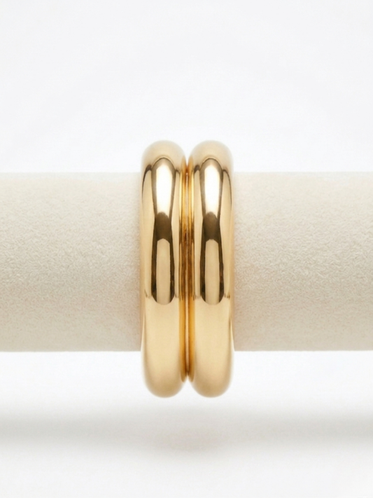 Primer plano de brazalete rígido dorado de diseño doble tubular con acabado pulido brillante de efecto espejo de Angel Salvaje.