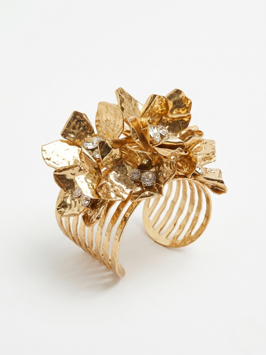 Vista en primer plano de brazalete rígido dorado ancho con ramillete tridimensional de flores texturizadas y pequeños cristales brillantes de Angel Salvaje.