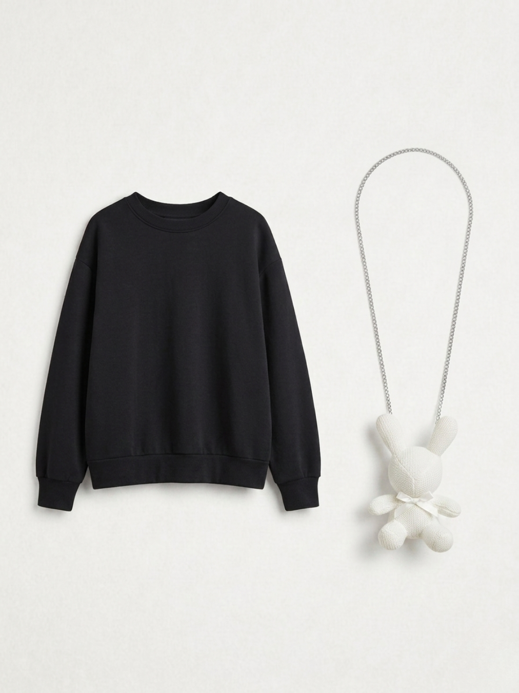 Sudadera negra y accesorio de peluche blanco presentados de forma individual sobre fondo neutro.