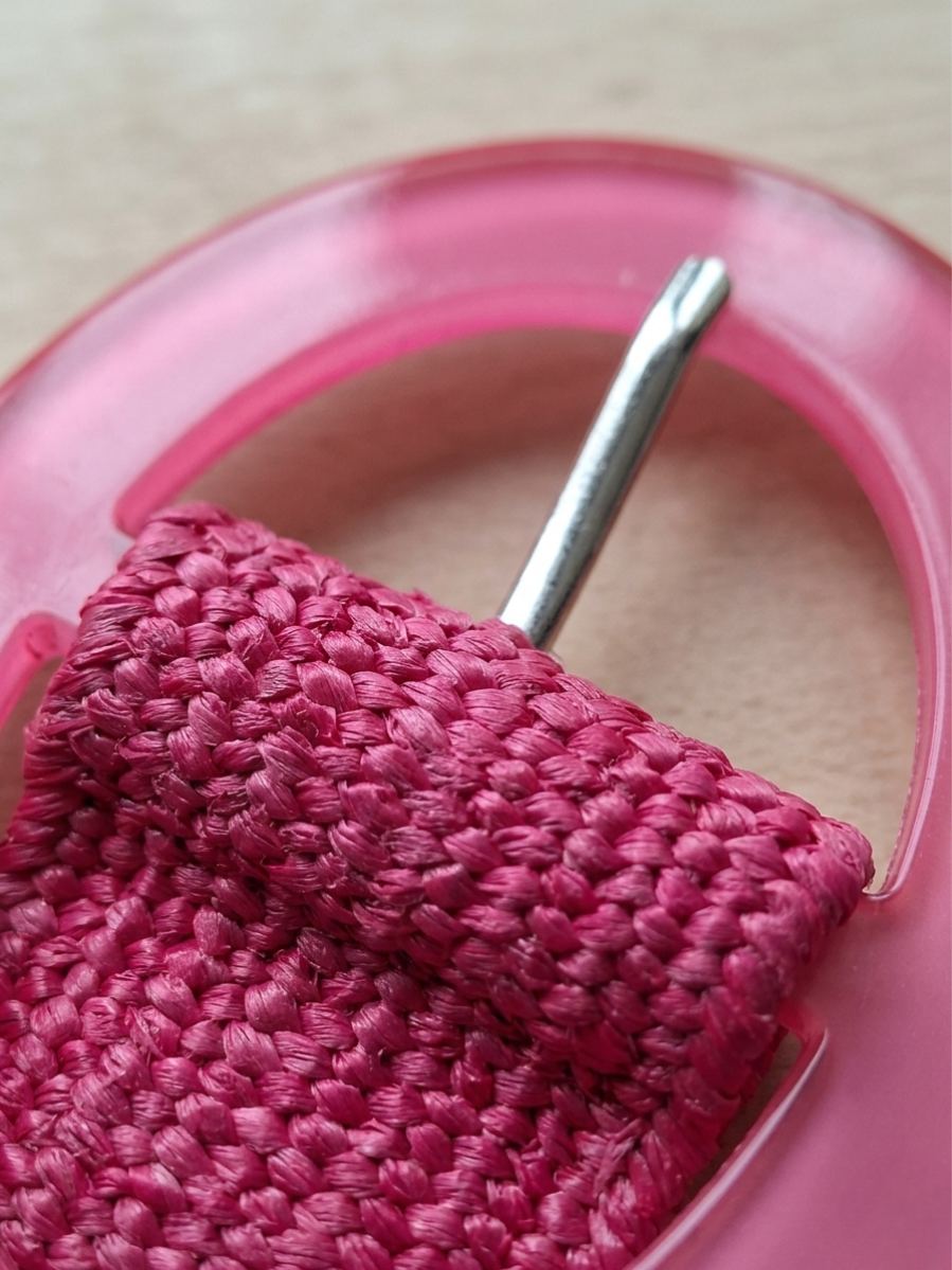 Primer plano de la hebilla redonda y el tejido trenzado del cinturón fucsia.