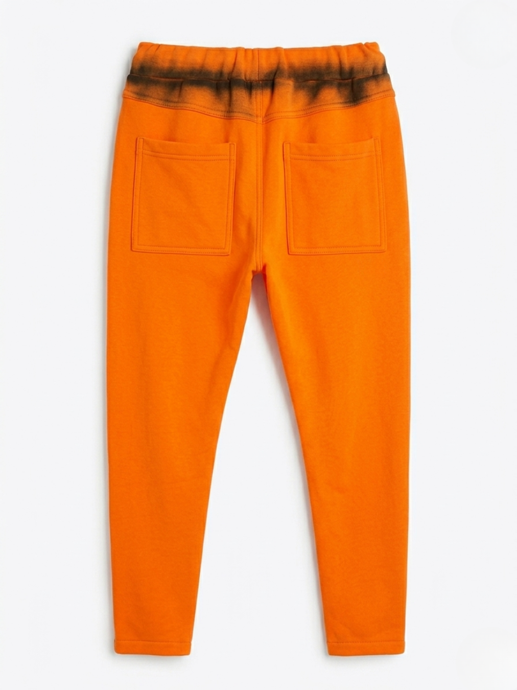 Parte posterior del pantalón naranja resaltando los bolsillos funcionales y el efecto spray negro.