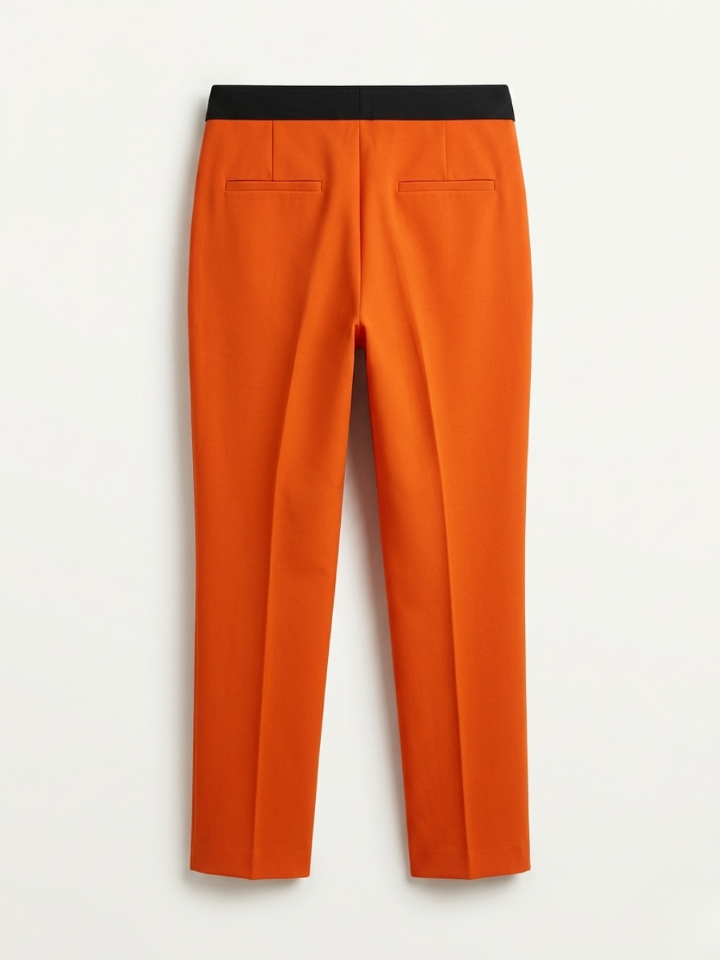 Detalle trasero de pantalón recto naranja con bolsillos decorativos de vivo y elástico negro.