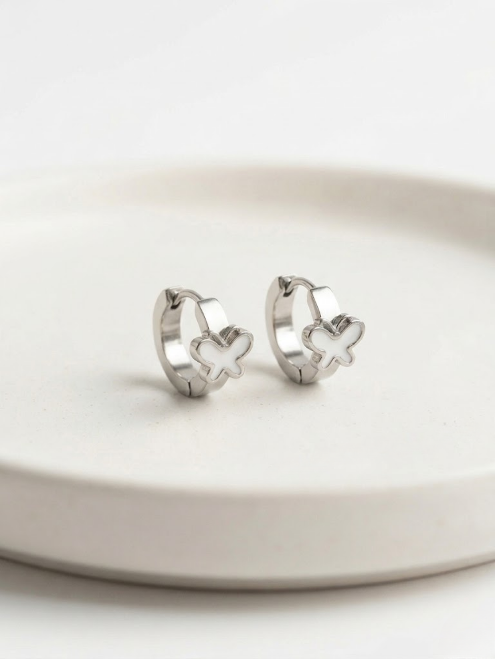 Pendientes mini aros plateados con mariposa blanca para look minimalista y juvenil.