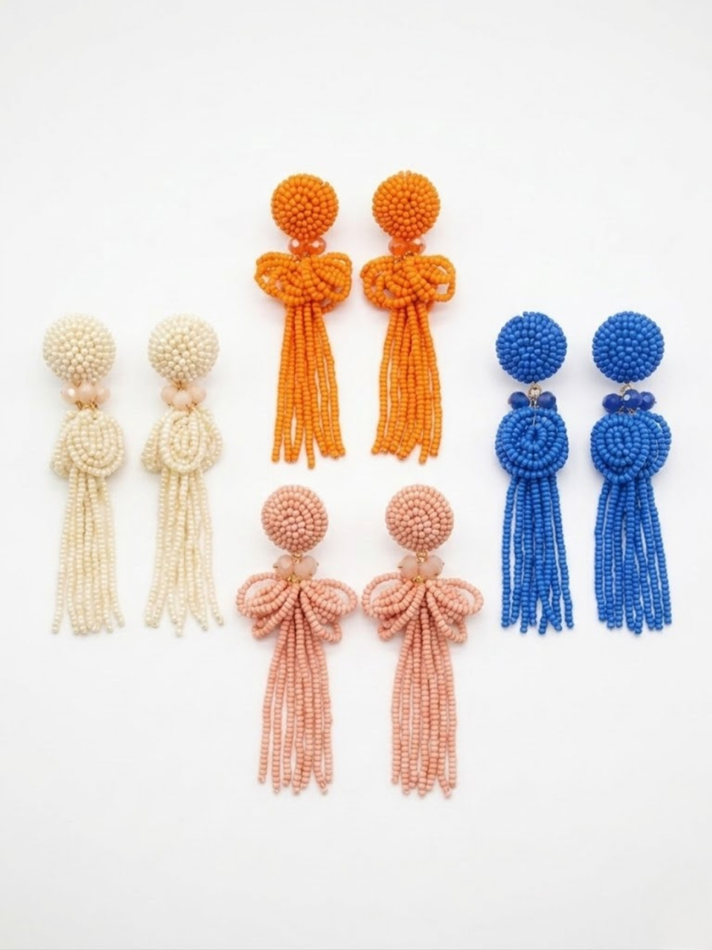 Muestra de las cuatro variantes de pendientes largos con flecos en cascada y detalle de lazo superior en colores blanco marfil, naranja, rosa palo y azul real de Angel Salvaje.