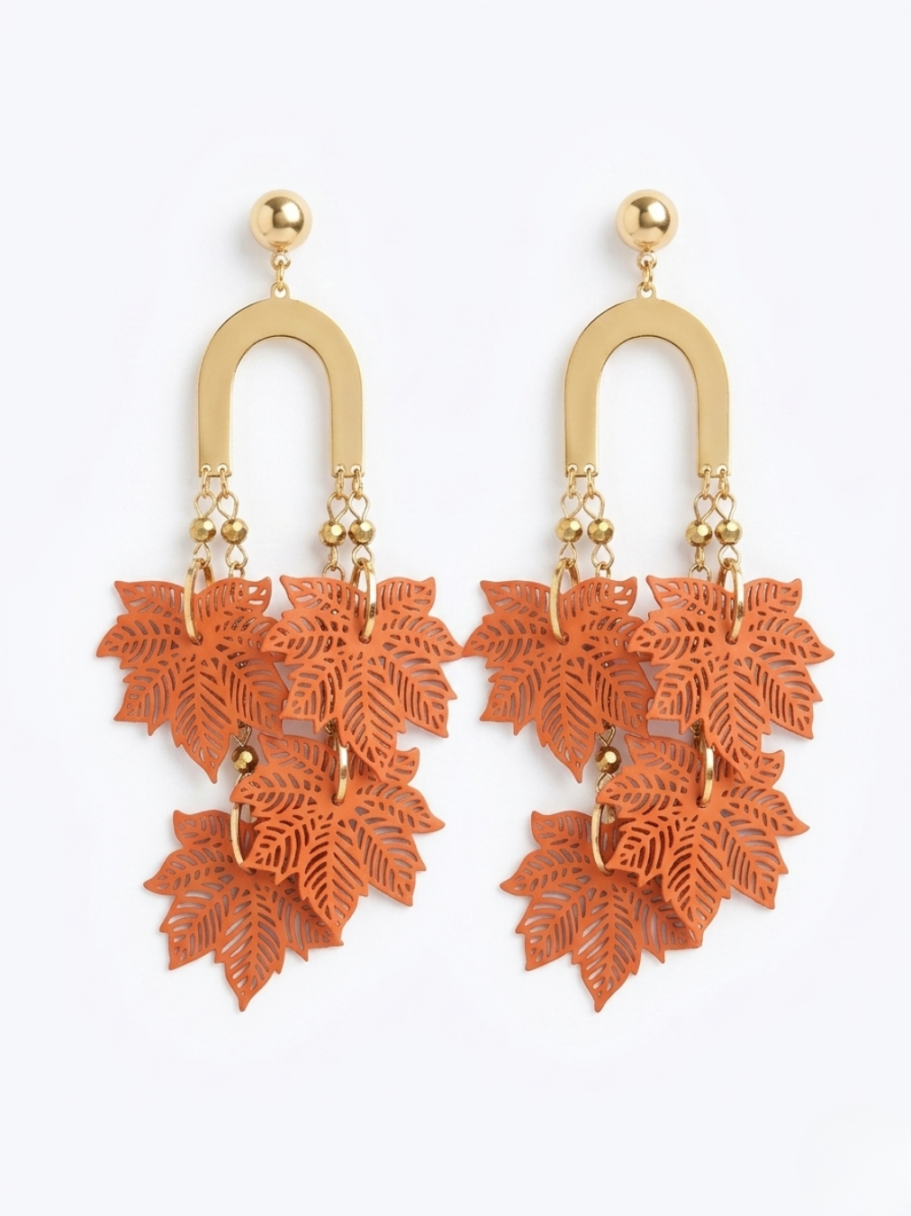 Pendientes maxi de diseño botánico con estructura dorada y ramillete de hojas troqueladas en color naranja vibrante.