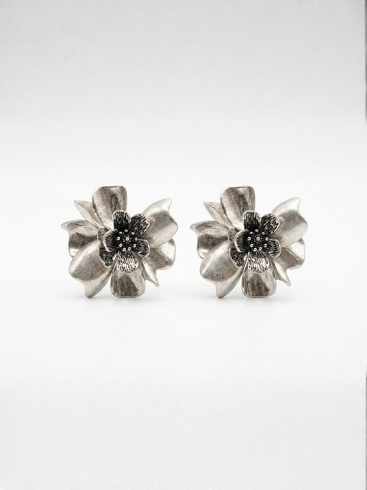 Vista frontal de pendientes grandes de botón con diseño de flor tridimensional y pétalos texturizados en tono plateado envejecido de Ángel Salvaje.