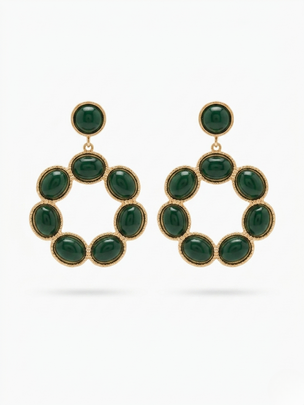 Vista frontal de pendientes grandes de silueta circular con cabujones lisos en color verde esmeralda y montura dorada texturizada de Ángel Salvaje.