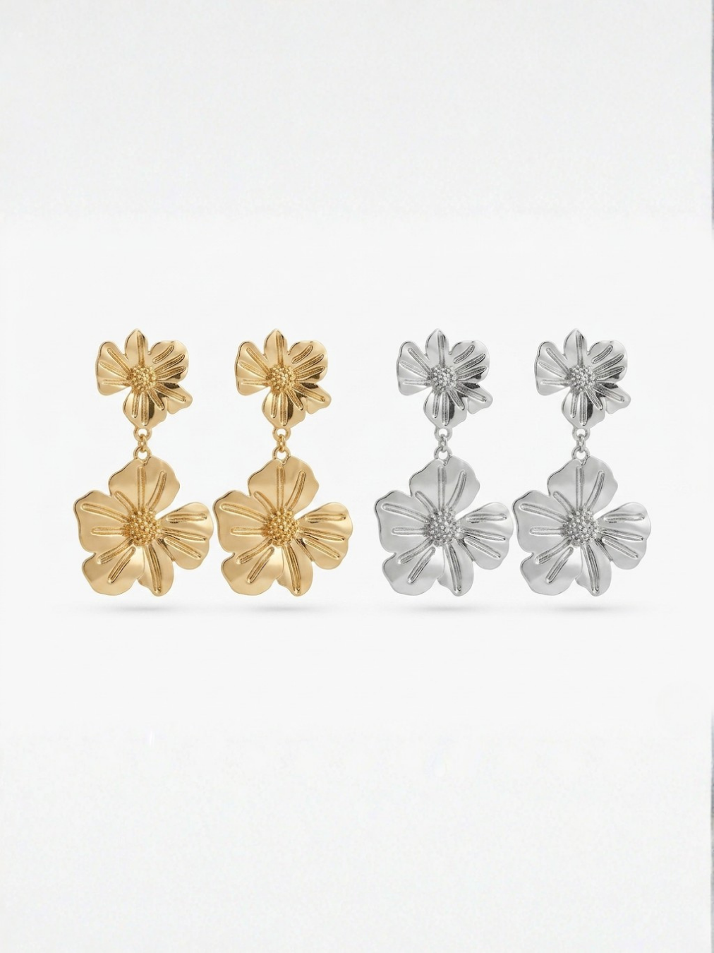 Presentación de las dos variantes de pendientes largos de doble flor con pétalos estriados y movimiento en colores dorado brillante y plateado pulido de Ángel Salvaje.