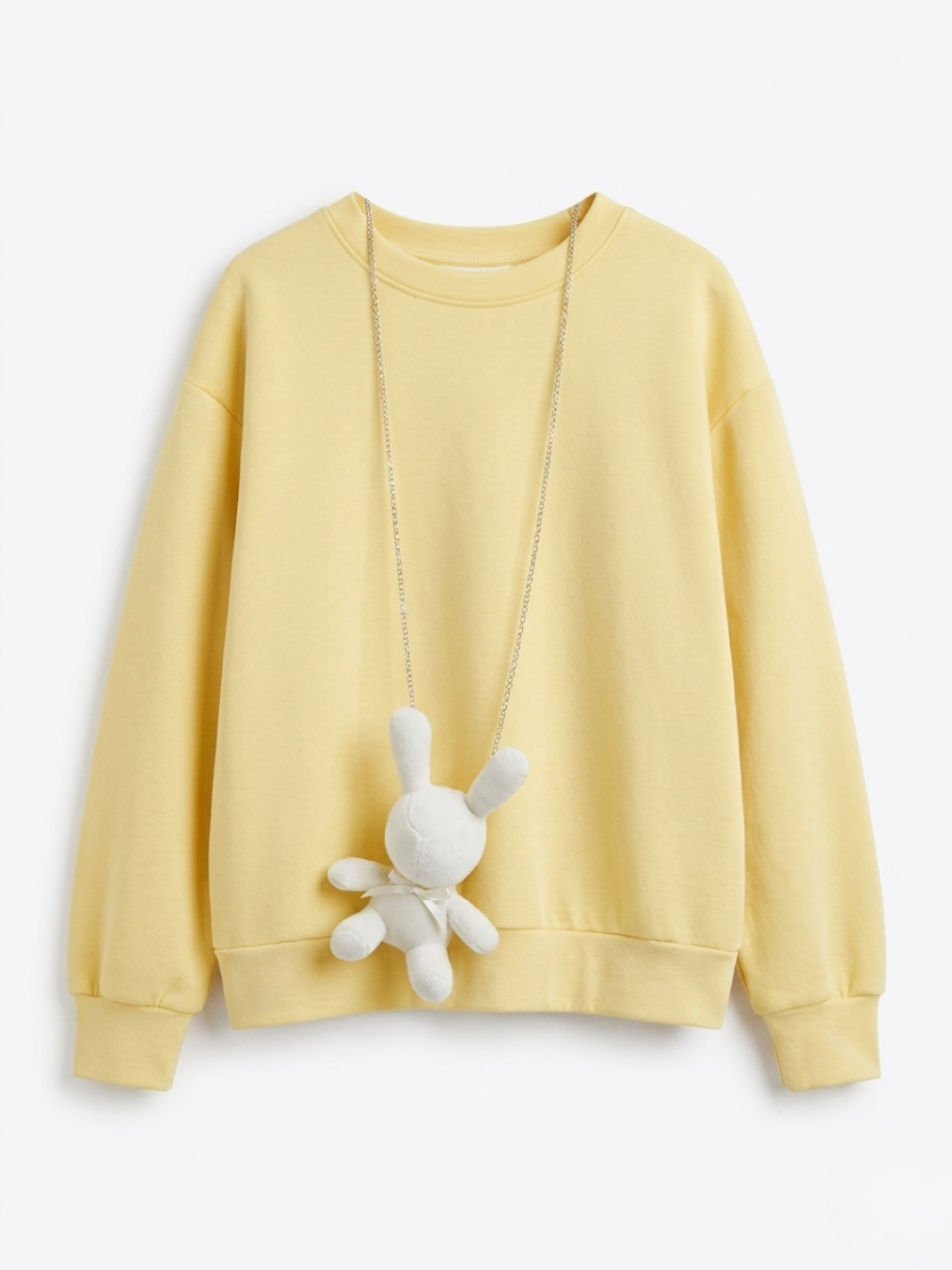 Sudadera color amarillo pastel con colgante de cadena y conejo de peluche blanco.